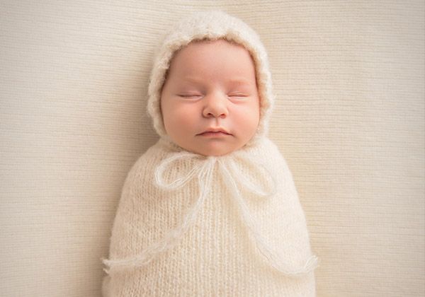 A sleeping newborn swaddled in a knit bonnet