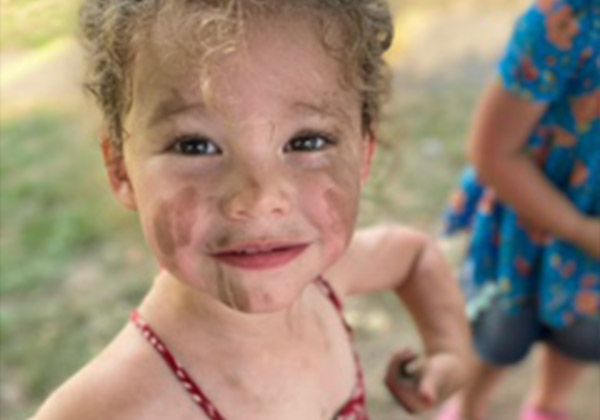 A curly-haired toddler smiling outdoors