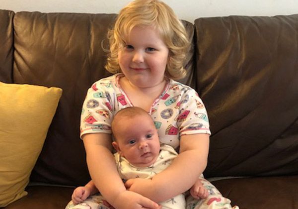 A toddler holding a newborn on a sofa